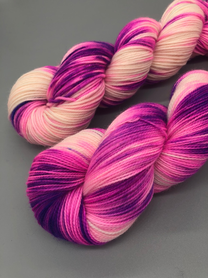 May include: A skein of yarn with pink, white, and purple stripes. The yarn is soft and fluffy, and it would be perfect for knitting or crocheting.