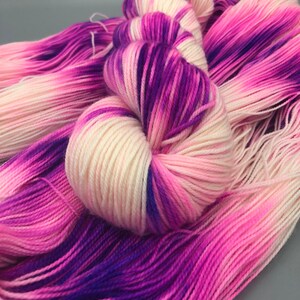 May include: A skein of yarn with a gradient of pink, white, and purple colors. The yarn is soft and fluffy, and it would be perfect for knitting or crocheting.