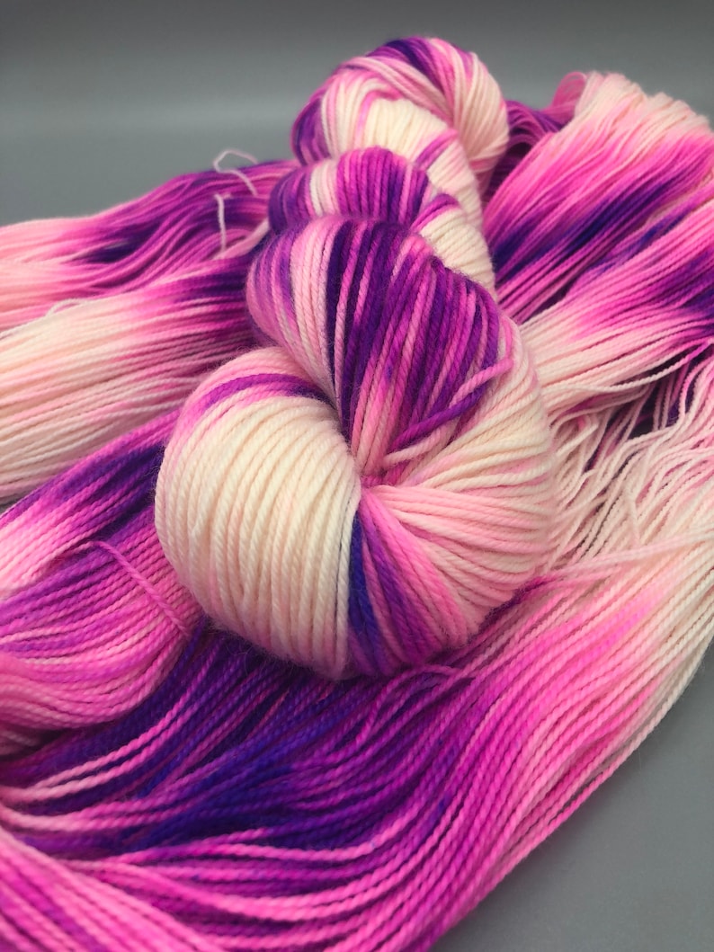 May include: A skein of yarn with a gradient of pink, white, and purple colors. The yarn is soft and fluffy, and it would be perfect for knitting or crocheting.