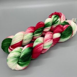May include: A skein of yarn in a red, green and white colourway. The yarn is twisted and folded, showing off the colour variations.