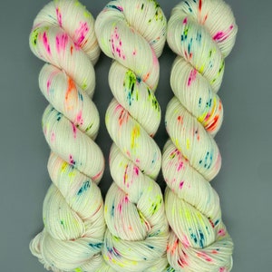Puede incluir: Tres ovillos de hilo blanco con motas de colores. El hilo es una mezcla de blanco, rosa, naranja, amarillo, verde, azul y turquesa.
