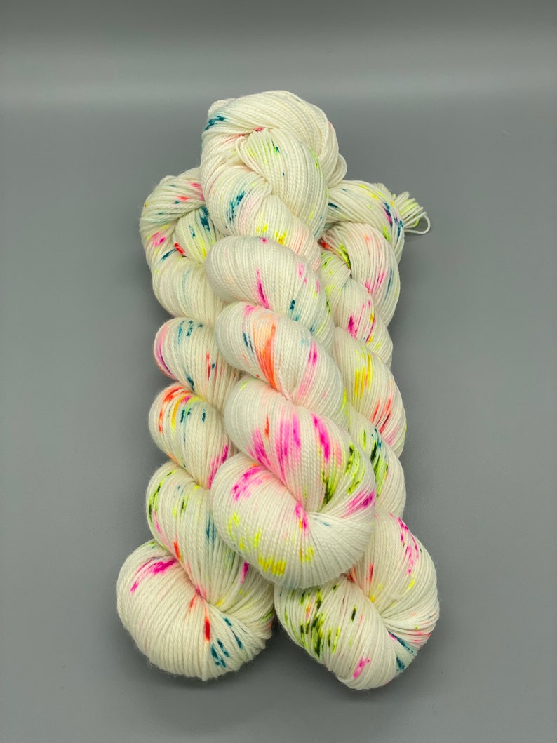 Puede incluir: Hilo blanco con motas de colores rosa, naranja, verde, azul y amarillo.