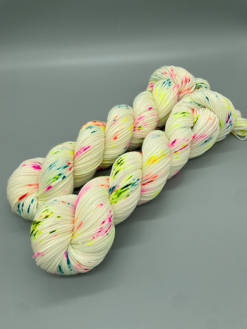 Puede incluir: Hilo blanco con motas de colores rosa, verde, azul y amarillo.