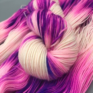 May include: A skein of yarn with a gradient of pink, white, and purple colors. The yarn is soft and fluffy, and it would be perfect for knitting or crocheting.