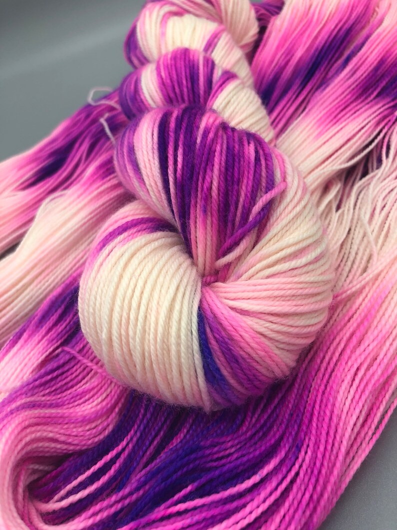 May include: A skein of yarn with a gradient of pink, white, and purple colors. The yarn is soft and fluffy, and it would be perfect for knitting or crocheting.
