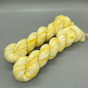 May include: Two skeins of yarn in a cream color with yellow speckles. The yarn is twisted together.