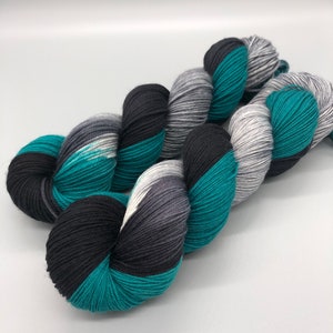 May include: Teal, black, and gray yarn skeins. The yarn is arranged in a loose, overlapping pattern.