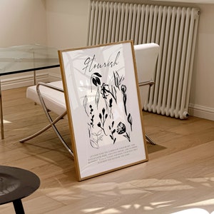 May include: A black and white art print with a gold frame. The print features a floral design with the word "Nourish" at the top. The text below the floral design reads "Let God tend the garden of your heart and watch faith, hope, and love appear, like flowers blooming in the sunlight, and look, you will flourish and never be the same."