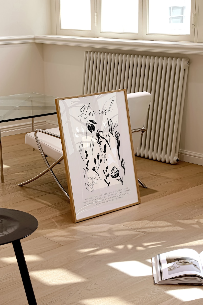 May include: A black and white art print with a gold frame. The print features a floral design with the word "Nourish" at the top. The text below the floral design reads "Let God tend the garden of your heart and watch faith, hope, and love appear, like flowers blooming in the sunlight, and look, you will flourish and never be the same."