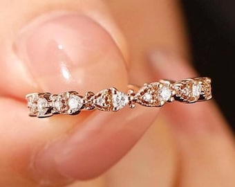 May include: Rose gold ring with a delicate design featuring alternating shapes and small, clear gemstones. The ring is held in a hand, showcasing its intricate details and sparkle. The text "PerfectLoverRing" is visible.