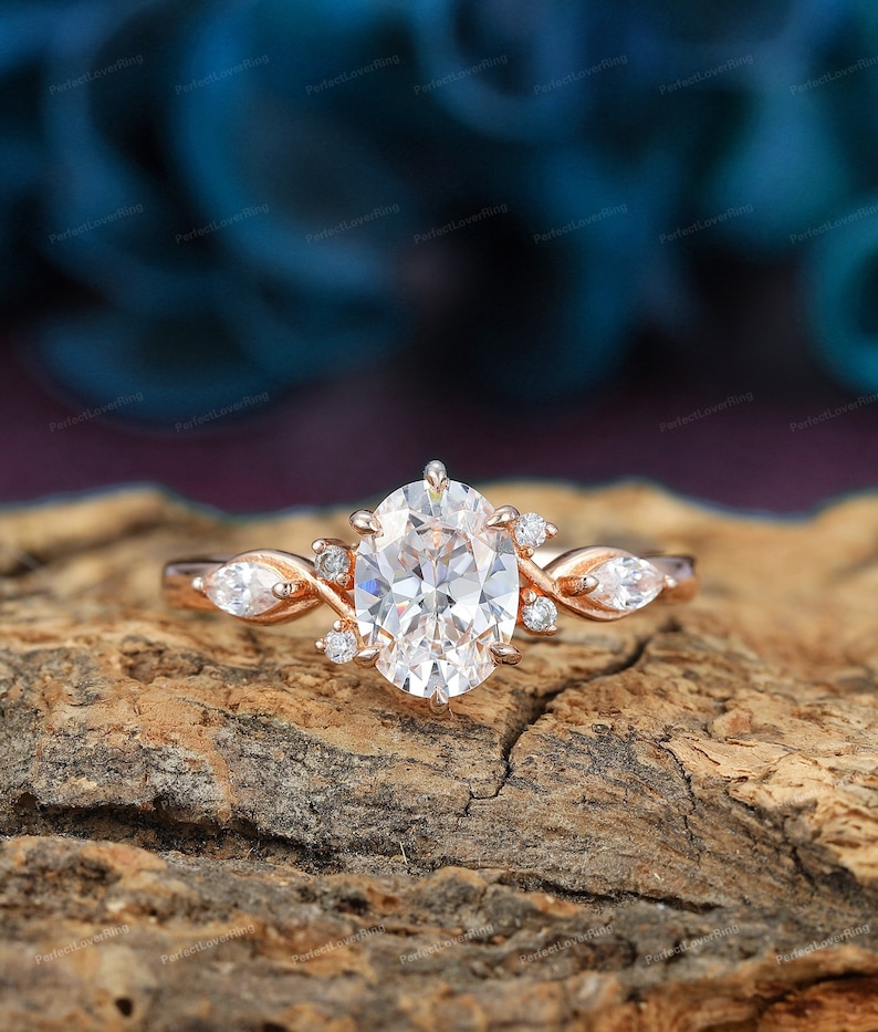 May include: Rose gold oval-cut diamond engagement ring with twisted band and marquise-shaped side stones. The center stone is a large, brilliant oval diamond, surrounded by smaller diamonds. The band is a delicate twisted design, with two marquise-shaped diamonds set on either side of the center stone. The ring is set on a rustic wooden surface.