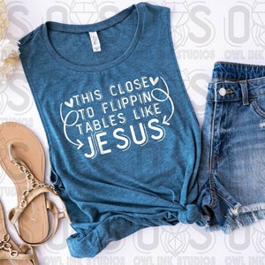 May include: A teal blue sleeveless tank top with the text "This close to flipping tables like Jesus" in white. The tank top is tied in a knot at the front.