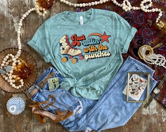May include: A teal blue t-shirt with a retro roller skate graphic and the text "Just rollin' with the punches".