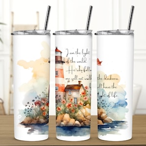 May include: A white tumbler with a watercolor illustration of a lighthouse, flowers, and a house. The text "I am the light of the world. He who follows me will not walk in darkness, but will have the light of life. John 8:12" is printed on the tumbler.