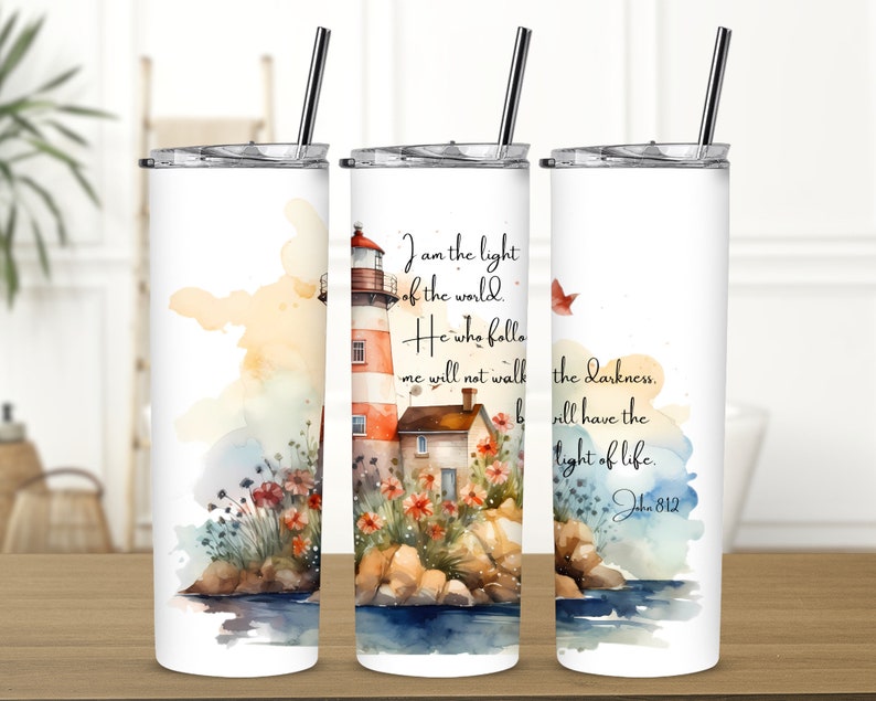 May include: A white tumbler with a watercolor illustration of a lighthouse, flowers, and a house. The text "I am the light of the world. He who follows me will not walk in darkness, but will have the light of life. John 8:12" is printed on the tumbler.