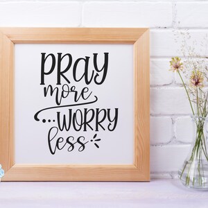 Może przedstawiać: Wydruk w ramie z tekstem "Pray more...worry less" czarnymi literami na białym tle. Rama jest z jasnego drewna, a wydruk leży na białej powierzchni.