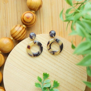 May include: A pair of gold hoop earrings with a tortoiseshell pattern. The earrings are on a wooden surface.