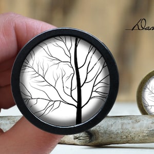 May include: A black and white image of a tree with bare branches, printed on a round, black, wooden button.