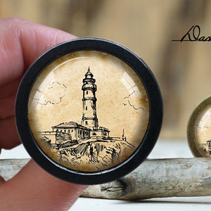 May include: A black and white illustration of a lighthouse on a beige background. The image is framed in a black circular frame.