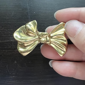 Può includere: Un fermaglio a forma di fiocco dorato, dal design semplice ed elegante.