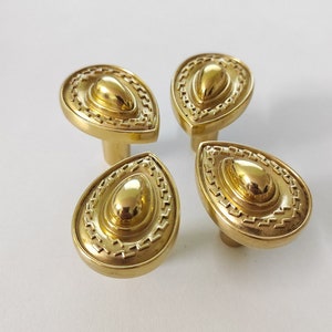 May include: Four gold-toned teardrop-shaped cabinet knobs with a decorative, raised, concentric circle design.