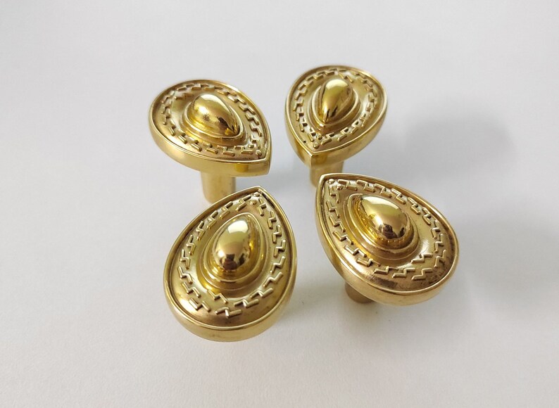 May include: Four gold-toned teardrop-shaped cabinet knobs with a decorative, raised, concentric circle design.