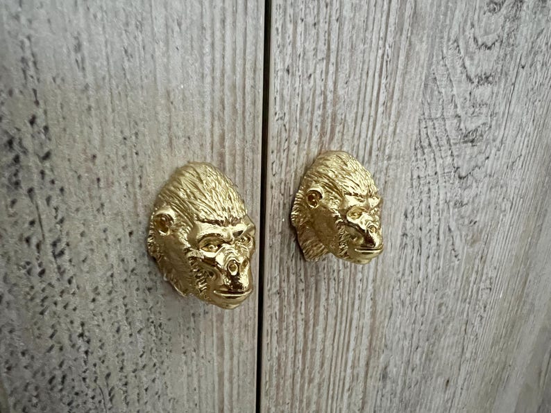 May include: Two gold-colored gorilla head cabinet door pulls. The pulls are detailed and realistic.