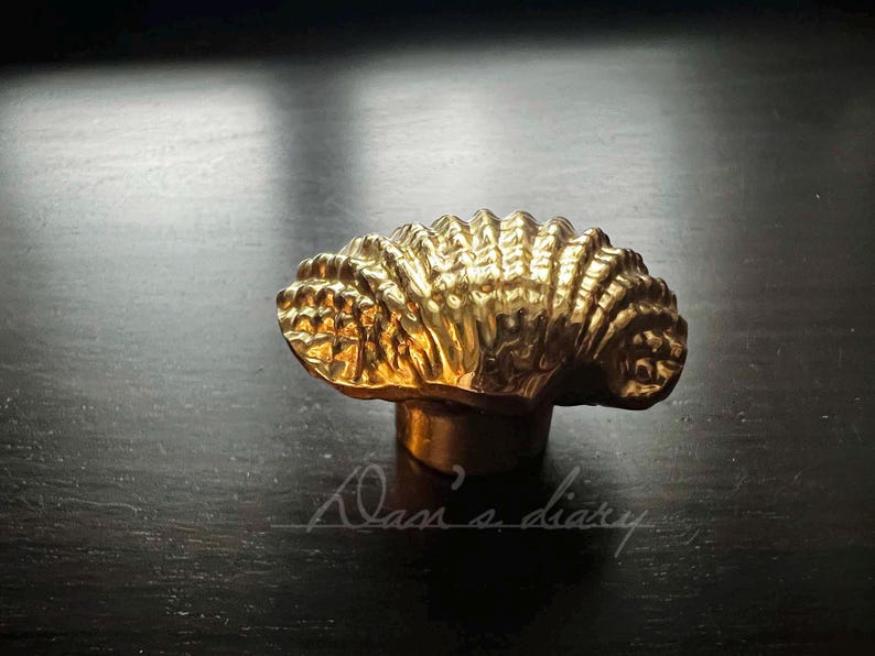 May include: A gold-colored bottle stopper shaped like a seashell. The stopper has a detailed, textured surface.