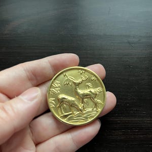 以下が含まれることがあります： 森の背景に2頭の鹿が浮き彫りになった、金色の金属製のピン