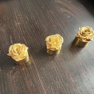 May include: Three gold-colored rose-shaped bottle stoppers. Each stopper features a detailed rose design with a gold finish.
