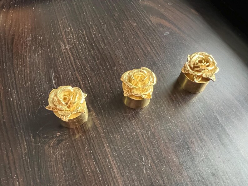 May include: Three gold-colored rose-shaped bottle stoppers. Each stopper features a detailed rose design with a gold finish.