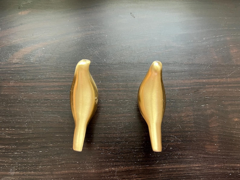 Pu&ograve; includere: Due ganci da parete a forma di uccello color oro.