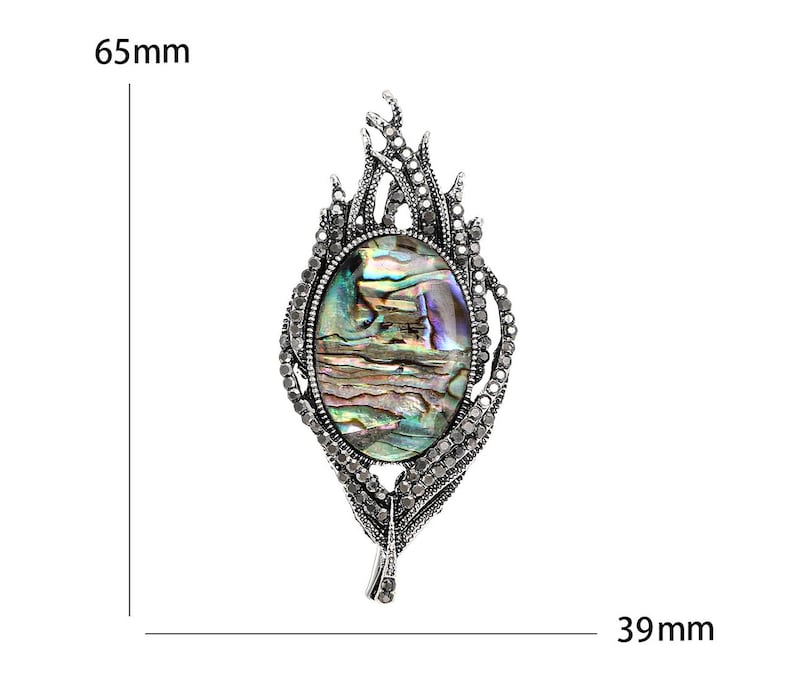 May include: An oval brooch with an abalone shell centre, set in an ornate silver-toned frame. The brooch is 6.5 cm long and 3.9 cm wide. The design features a detailed, textured pattern with small crystals, creating a vintage aesthetic. A statement piece.