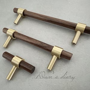 Pode incluir: Três botões de armário de madeira com detalhes em latão. Os botões são de tamanhos diferentes e têm um acabamento em madeira escura.