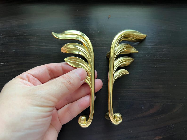 May include: Two gold-toned leaf-shaped cabinet pulls with a decorative scroll design at the bottom.
