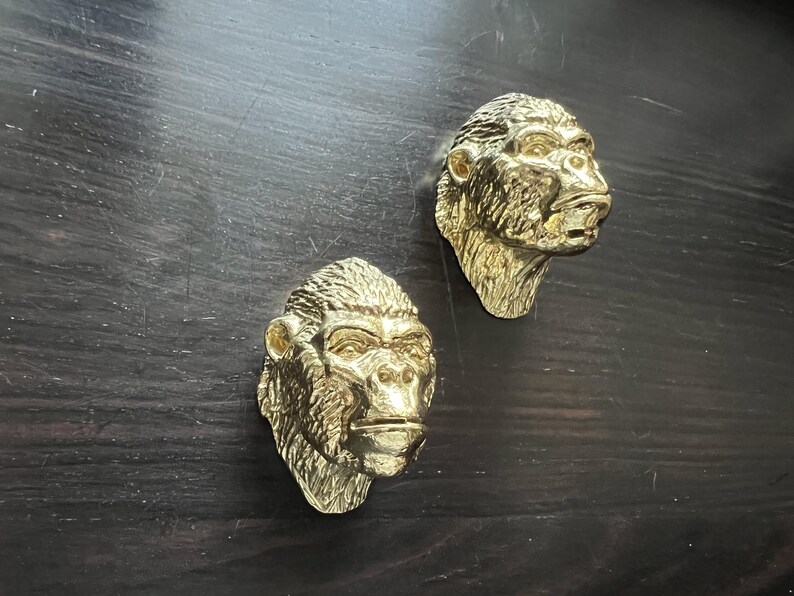 May include: Two gold-colored gorilla head sculptures. The sculptures are detailed and realistic, with textured fur and expressive faces.