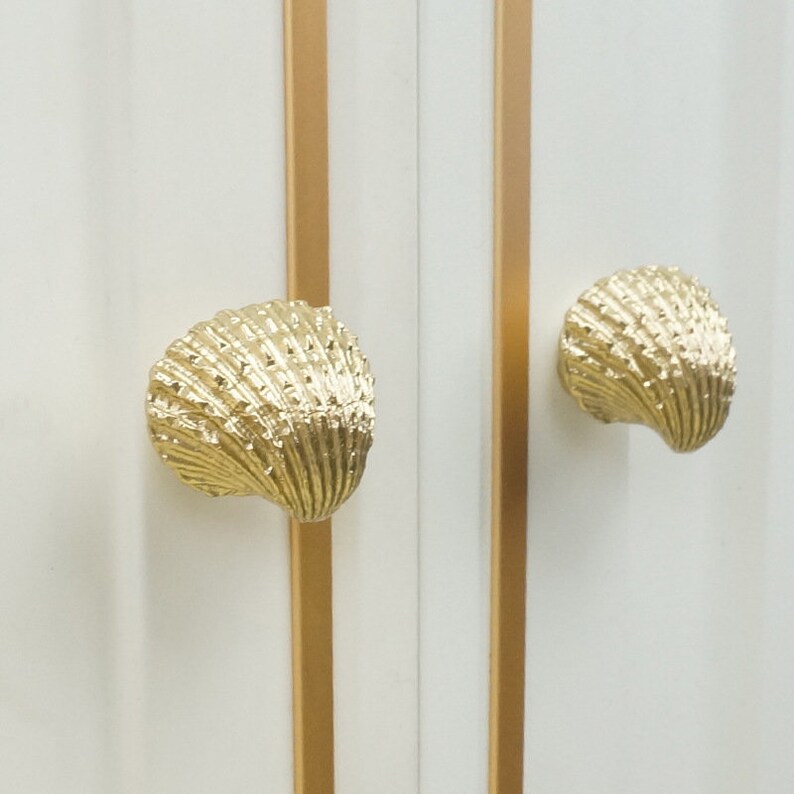May include: Two gold seashell-shaped cabinet knobs with a textured surface.