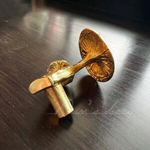 May include: A gold-toned metal door handle with a decorative mushroom design. The handle has a round base and a curved stem.