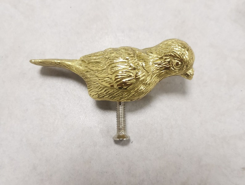 Puede incluir: Una figurita de p&aacute;jaro de metal de color dorado con un dise&ntilde;o detallado. El p&aacute;jaro tiene una cabeza peque&ntilde;a y redonda con un pico y un cuerpo largo y delgado. La figurita est&aacute; montada en un tornillo de metal.