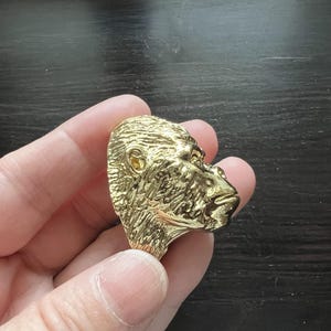 May include: A gold-colored metal ring featuring a detailed, three-dimensional gorilla head design.