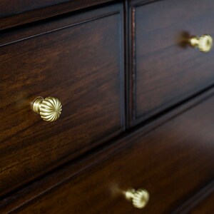 Puede incluir: Una c&oacute;moda de madera marr&oacute;n oscuro con tres cajones. Cada caj&oacute;n tiene una perilla de lat&oacute;n con un dise&ntilde;o decorativo.