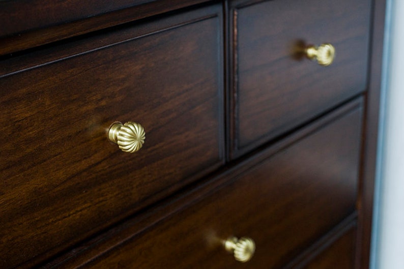 Puede incluir: Una c&oacute;moda de madera marr&oacute;n oscuro con tres cajones. Cada caj&oacute;n tiene una perilla de lat&oacute;n con un dise&ntilde;o decorativo.