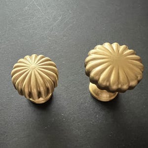 Puede incluir: Dos pomos de armario de color dorado con un dise&ntilde;o acanalado en forma de sol. Los pomos son de diferentes tama&ntilde;os.