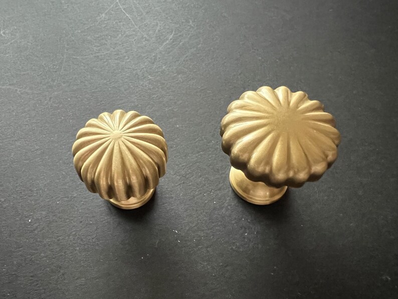 Puede incluir: Dos pomos de armario de color dorado con un dise&ntilde;o acanalado en forma de sol. Los pomos son de diferentes tama&ntilde;os.