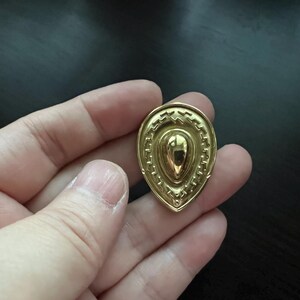 May include: A gold-colored pendant shaped like a teardrop with a textured, geometric design.