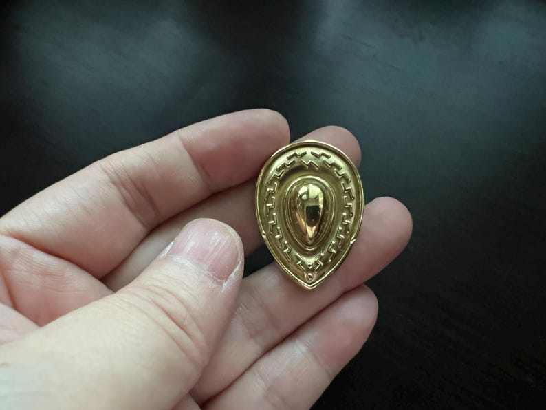 May include: A gold-colored pendant shaped like a teardrop with a textured, geometric design.