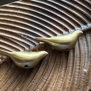 K&ouml;nnte beinhalten: Zwei goldene Vogel-f&ouml;rmige R&auml;ucherst&auml;bchenhalter auf einer braunen Holzoberfl&auml;che.