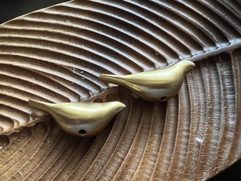 K&ouml;nnte beinhalten: Zwei goldene Vogel-f&ouml;rmige R&auml;ucherst&auml;bchenhalter auf einer braunen Holzoberfl&auml;che.