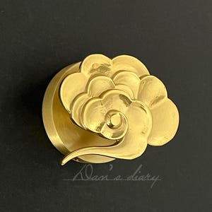 May include: A decorative object in the shape of a cloud, finished in a gold colour. The design incorporates layered, swirling shapes with a smooth, polished surface. The object is set against a dark background, with the text "Alan's diary".