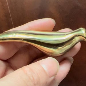 May include: A gold-coloured bird figurine with a smooth, shiny finish. The bird is depicted in a flying pose with its wings outstretched.